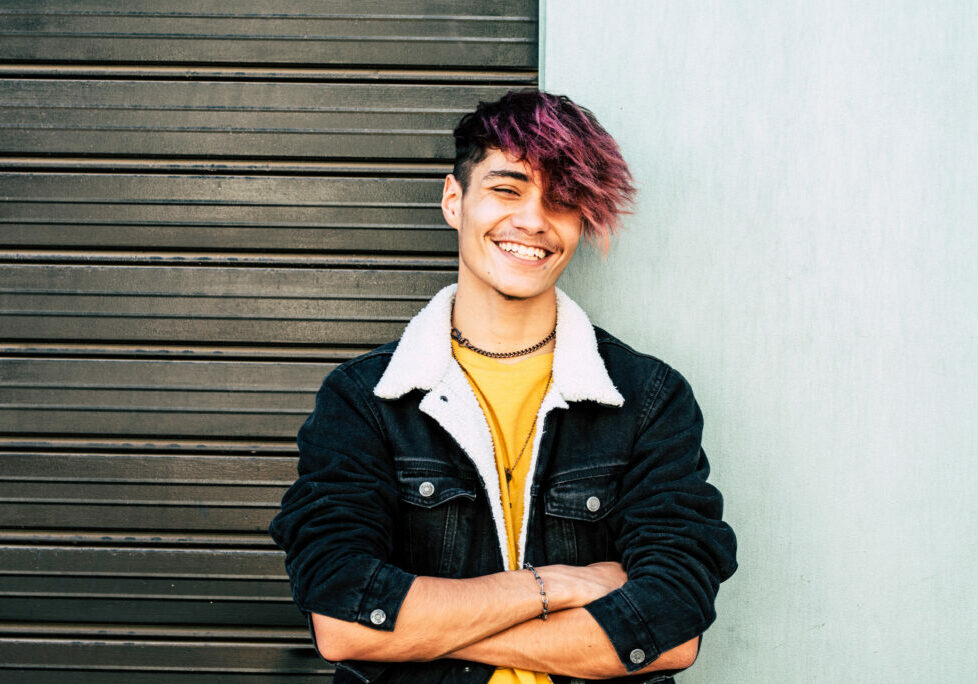 Cheerful portrait of caucasian young man teenager smiling at the camera - two colors background gray and white - urban people style having fun in outdoor
